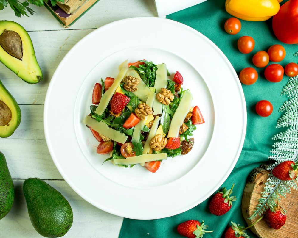 top view of fresh salad with parmesan cheese avocado walnuts cherry tomatoes and strawberries in a white bowl нутриціологиня